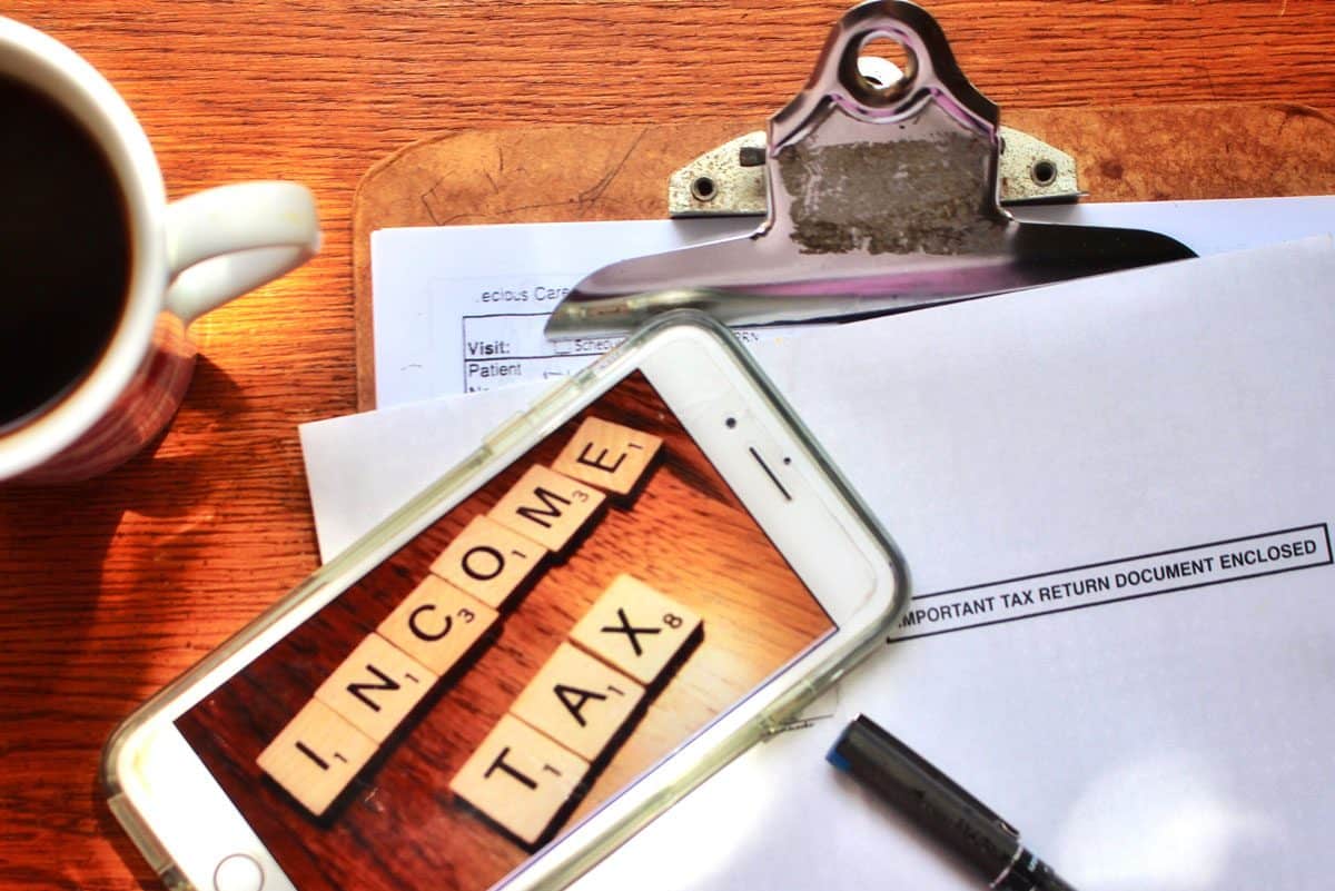 items on a desk: iras tax filing papers, coffee mug and a mobile phone showing image of tiles spelling income tax