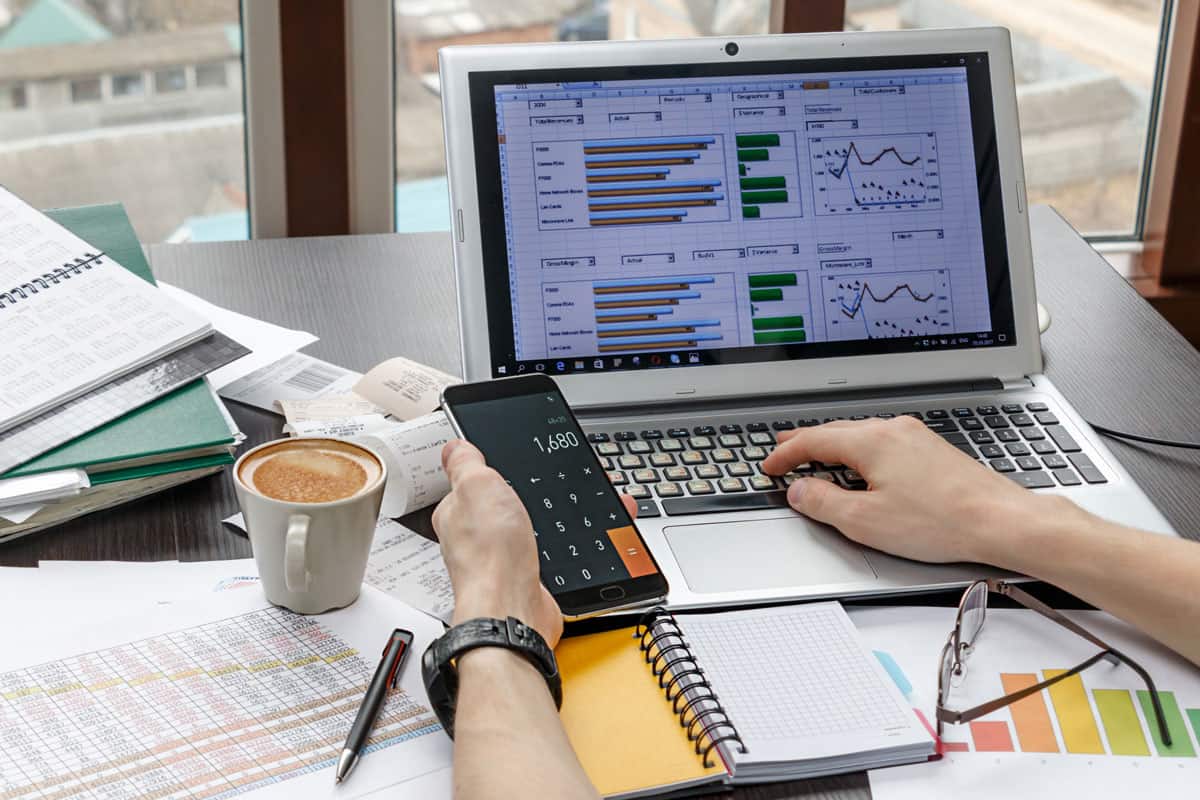 accountant holding a calculator and preparing income tax calculations for submission to IRAS, various tax documents and coffee mug on desk