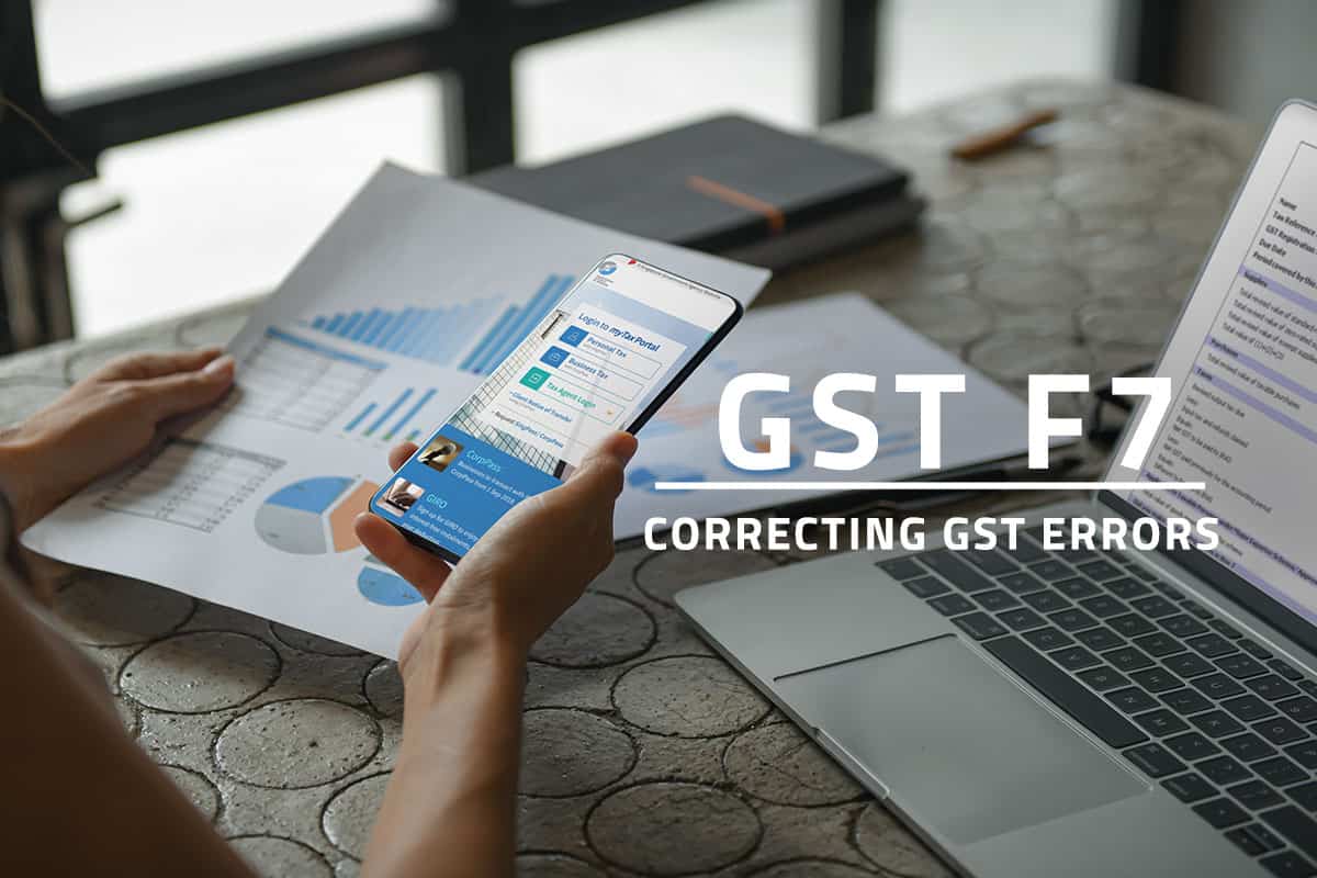 White text: GST F7 Correcting GST Errors over background of woman holding a mobile phone and logging in to the IRAS mytax portal. A nearby laptop on the table shows the GST F7 tax e-form