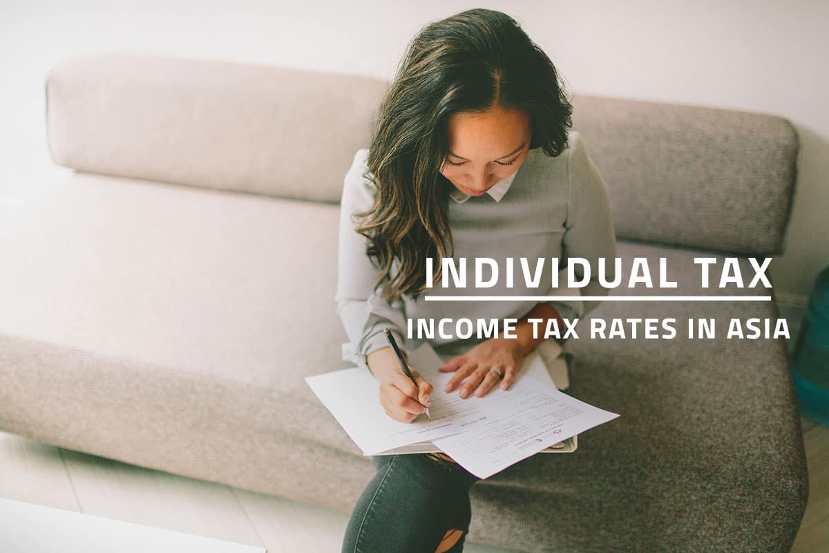 words individual tax income tax rates in asia over background of woman reviewing her personal tax documents while seated on a couch