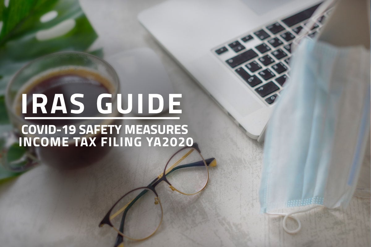 Words: IRAS Guide Covid-19 Safety Measures Income Tax Filing YA2020 against background of a coffee cup, glasses, laptop and a surgical face mask on a white table