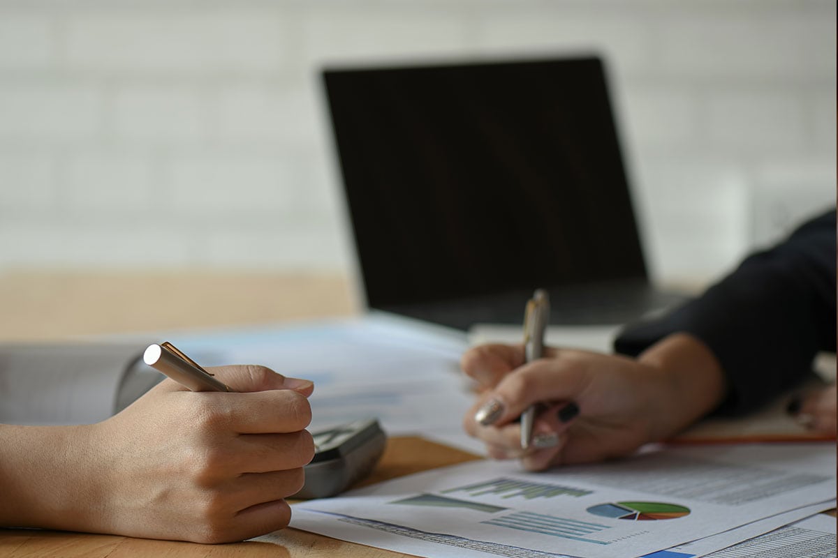 two accountants analysing financial reports on a desk with an unused laptop in the background