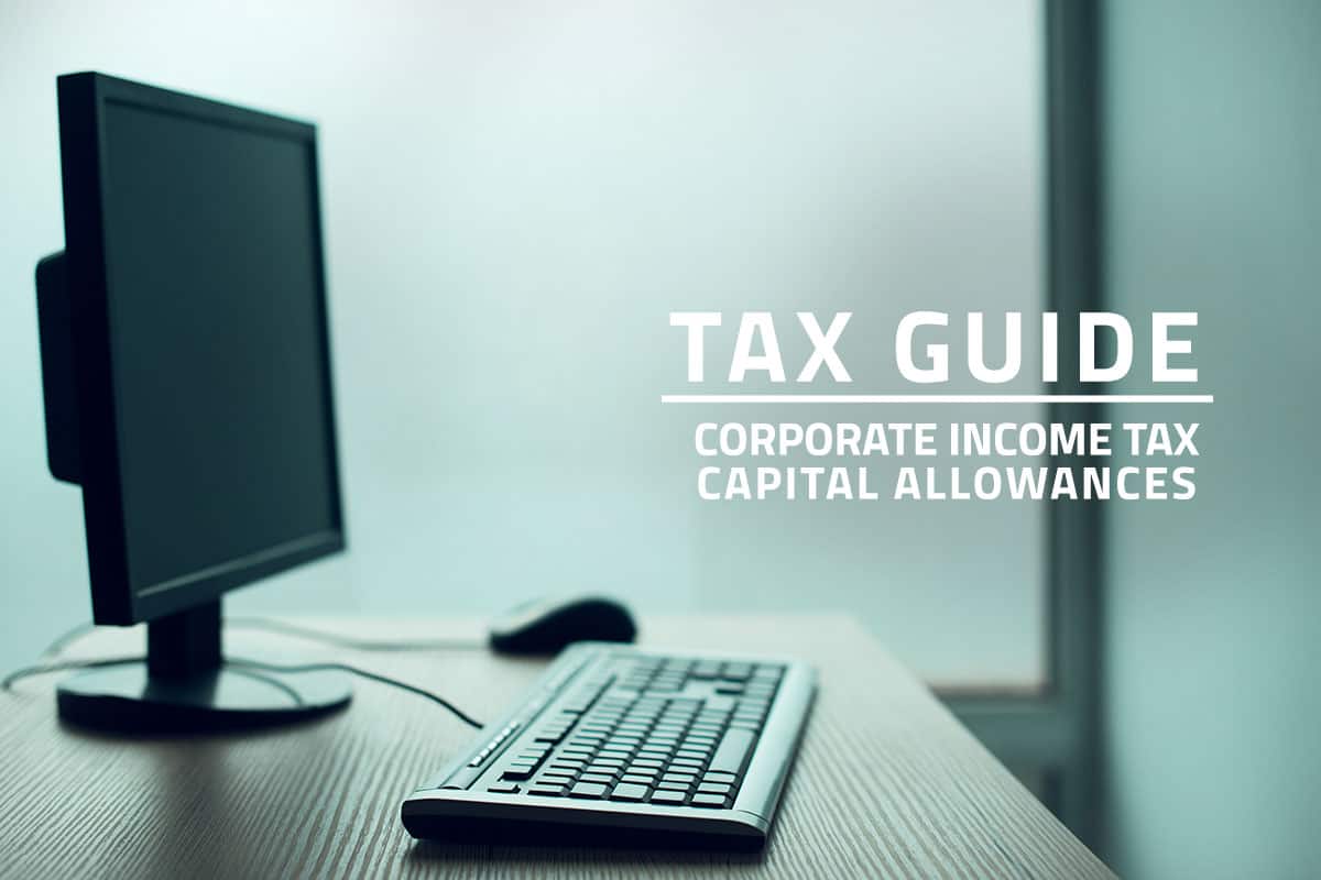 Words tax guide corporate income tax capital allowances against background of a desktop computer, mouse and keyboard on a wooden table.